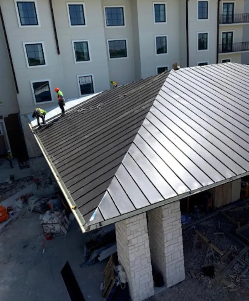 Crew installing standing seam metal roof panels on a commercial project in Bethany